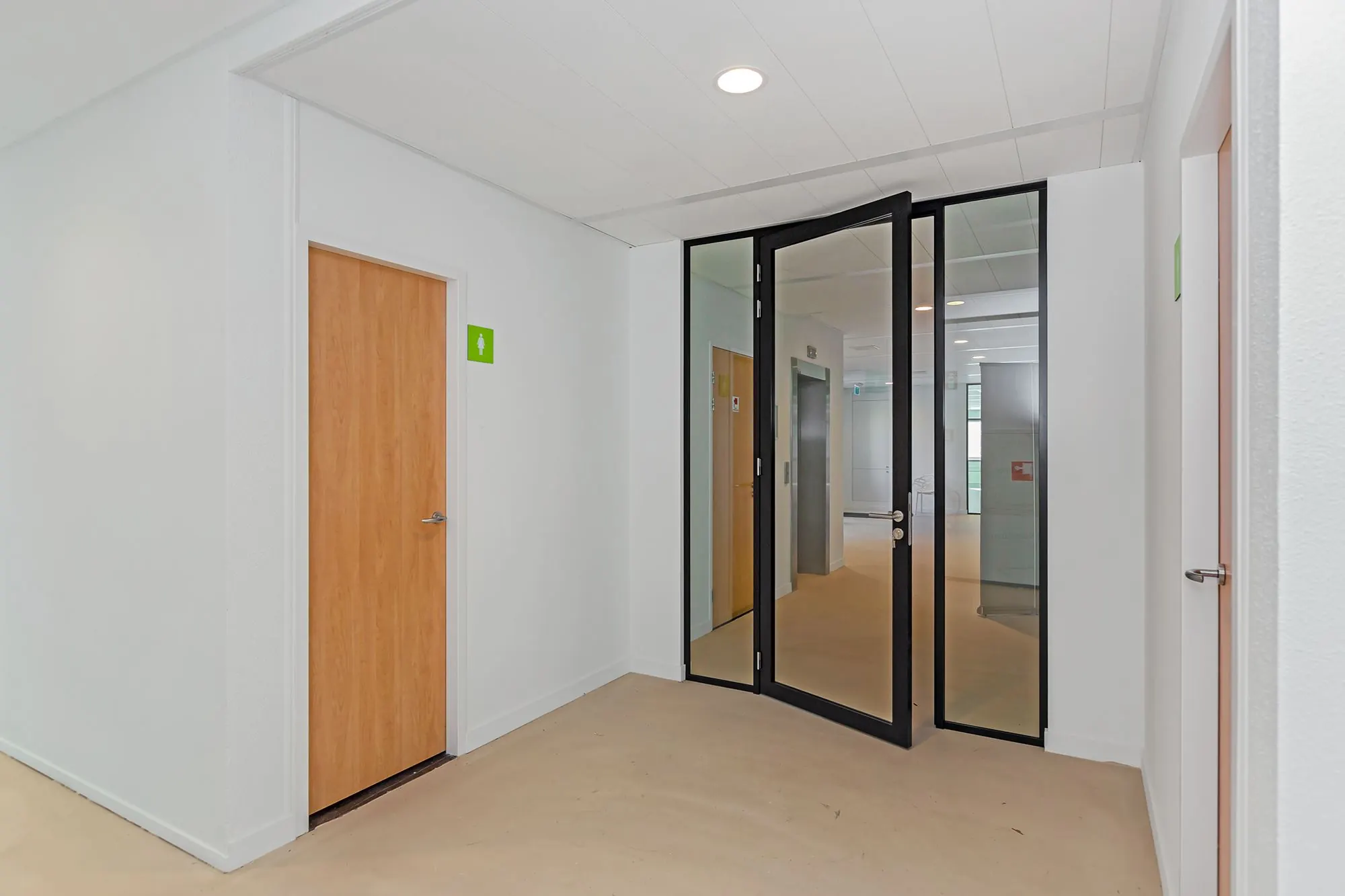 Moderne gang met houten deuren naar toiletten en een open glazen deur in een kantoorpand aan de Boris Pasternaklaan.